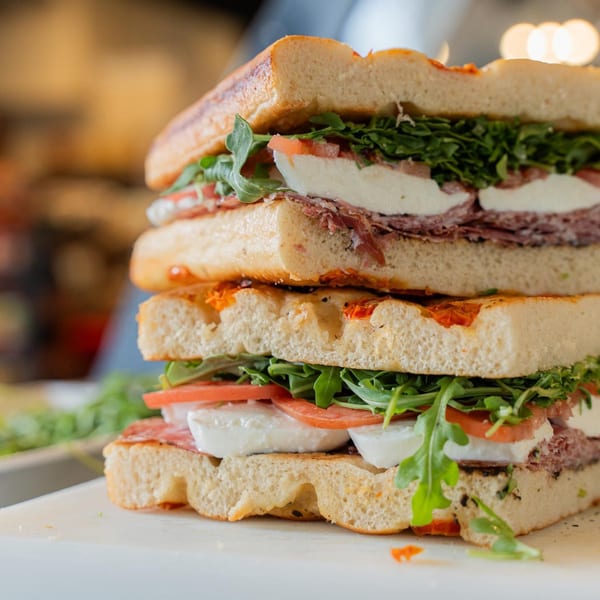Stacked Italian sandwich with salami, mozzarella, tomatoes, and arugula on focaccia bread.