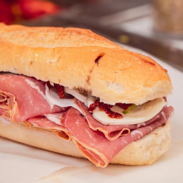 A close-up of an Italian sub sandwich with prosciutto, mozzarella, and sun-dried tomatoes.