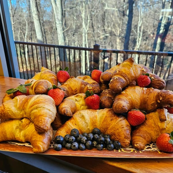 A large platter of golden croissants, fresh strawberries, and blueberries on a wooden table.