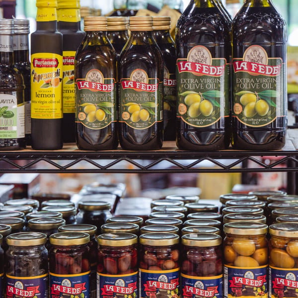 Shelves filled with various Italian olive oils and jars of olives, showcasing Taste of Italy's products.