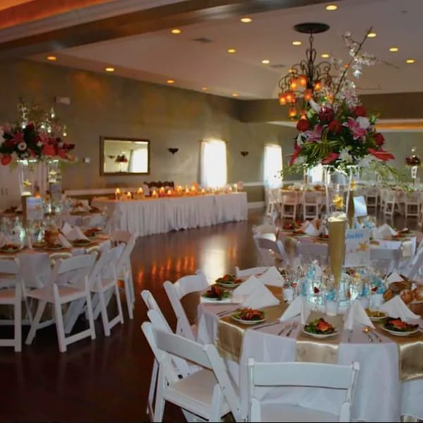Elegant Italian restaurant dining room set for an event with round tables, white chairs, and floral centerpieces.