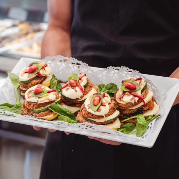 A server holds a tray of Italian appetizers with fried eggplant, zucchini, cheese, and cherry tomatoes.