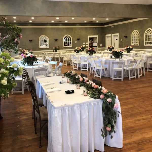 A Taste of Italy dining room set for an event with white tables, chairs, and floral centerpieces.