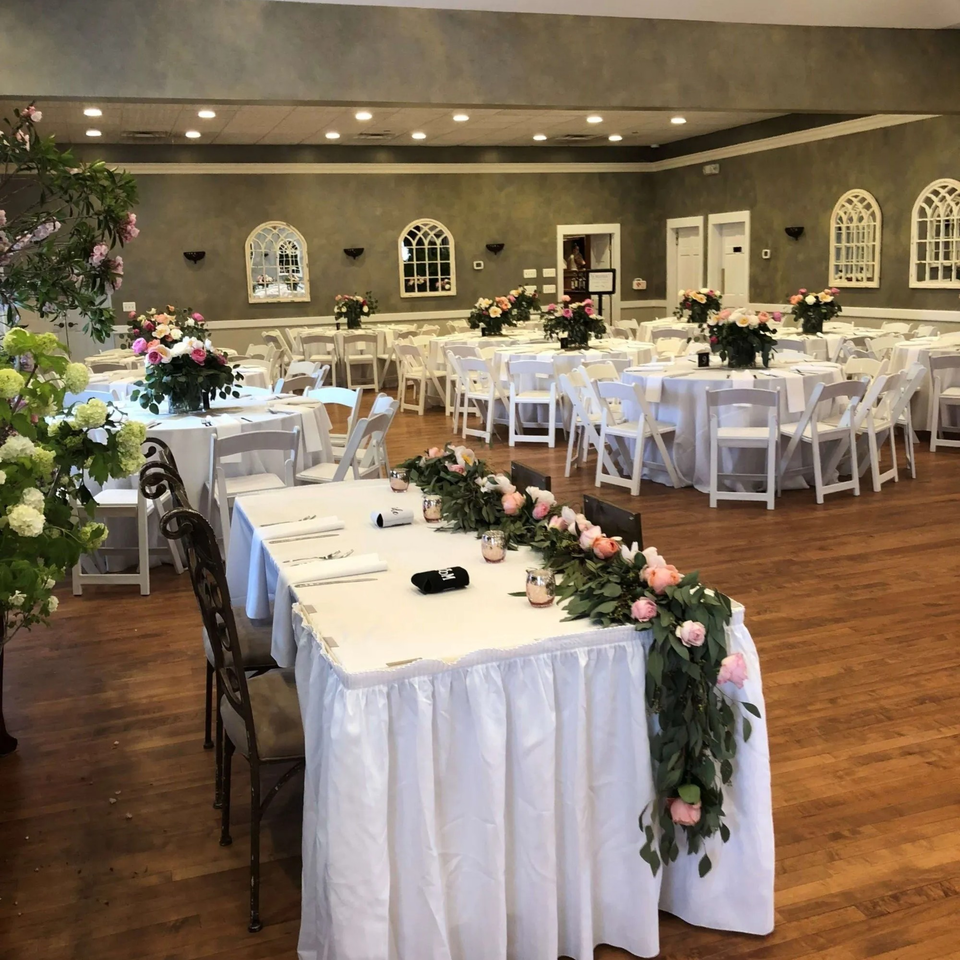 A Taste of Italy dining room set for an event with white tables, chairs, and floral centerpieces.