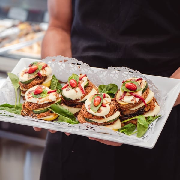 A server holds a tray of Italian appetizers with fried eggplant, cheese, zucchini, and cherry tomatoes.