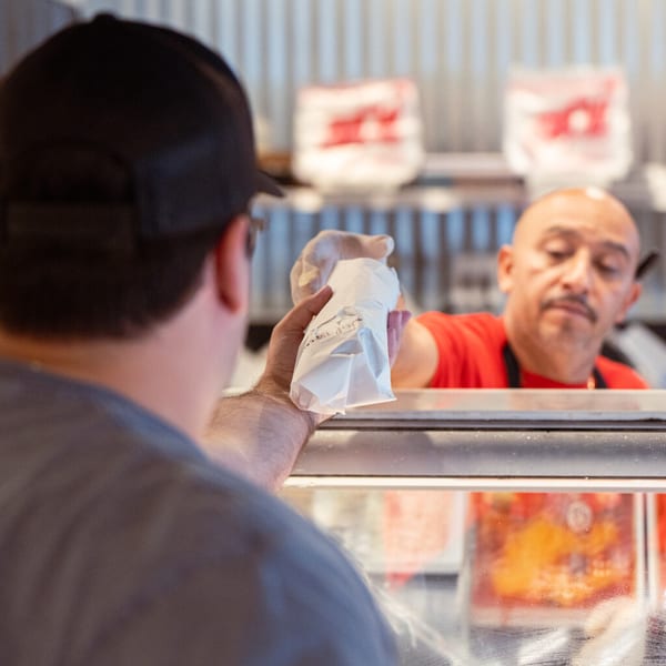 A customer receives a wrapped sandwich from a Taste of Italy employee behind a counter.