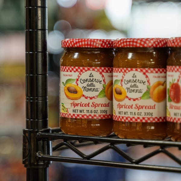 Jars of "Le Conserve della Nonna" apricot and strawberry spread on a black wire shelf.