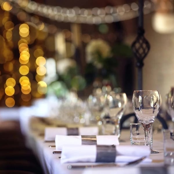 Elegantly set dining table with wine glasses, white napkins, and blurred golden lights in the background.