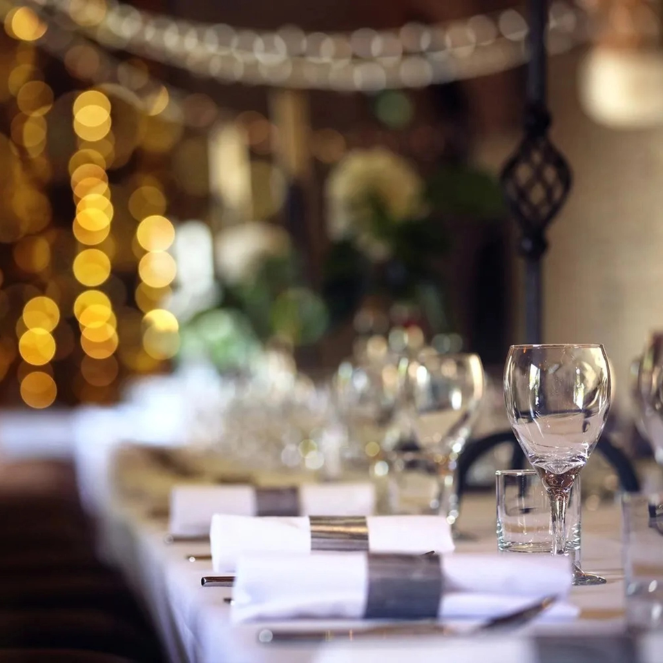 Elegantly set dining table with wine glasses, white napkins, and blurred golden lights in the background.