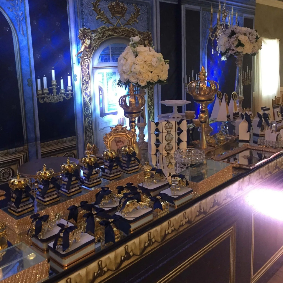 A luxurious blue and gold dessert table with white floral arrangements and crown decorations.
