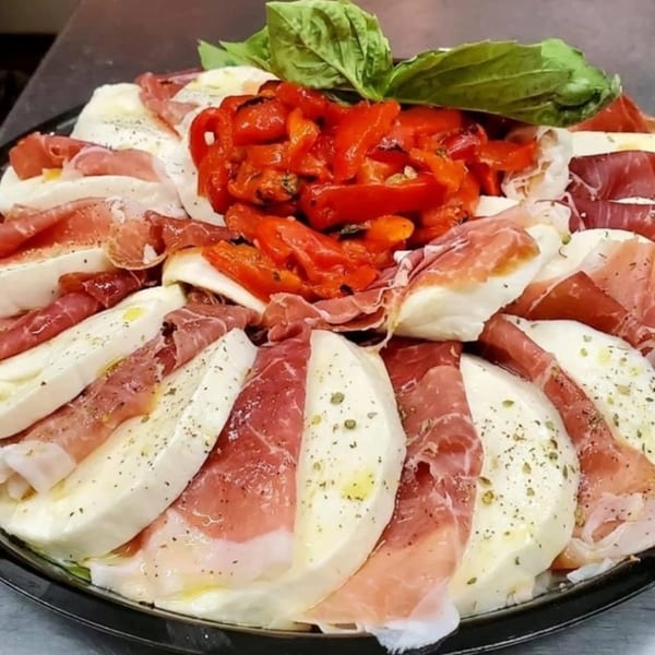 A platter of Italian antipasto with sliced mozzarella, prosciutto, roasted red peppers, and basil.