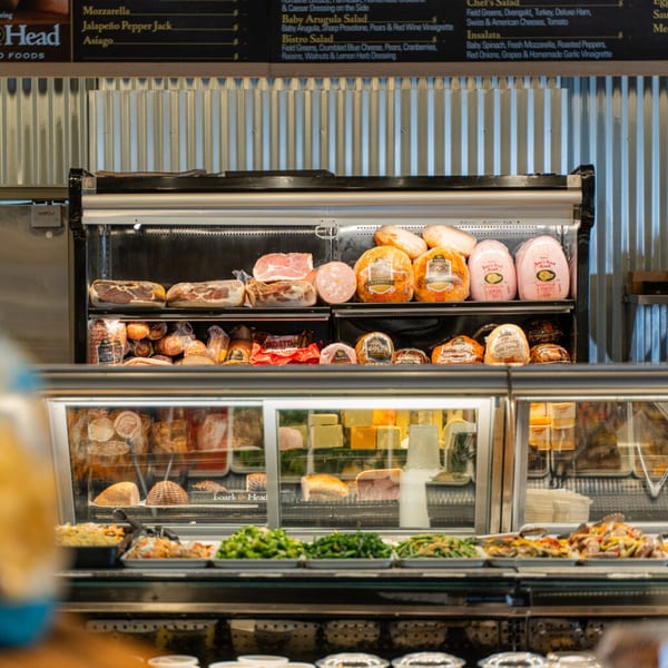 Deli counter at Taste of Italy, showcasing various meats, cheeses, and prepared salads.
