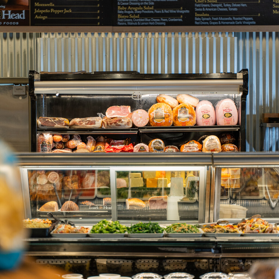 Deli counter at Taste of Italy, showcasing various meats, cheeses, and prepared salads.