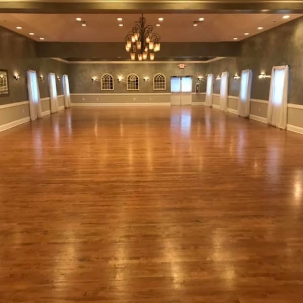 Empty ballroom with hardwood floors, arched windows, and a large chandelier at Taste of Italy.